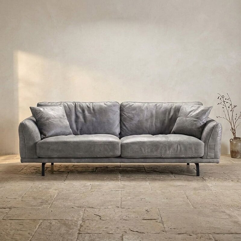Ein luxuriöses graues Ledersofa in einem minimalistischen Wohnzimmer mit natürlichem Lichteinfall und schlichter Dekoration – perfekt für stilvolle und gemütliche Sitzecken.