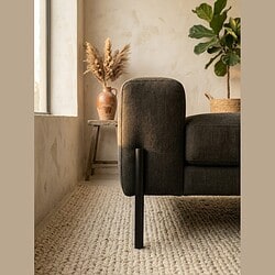 Moderne zwarte stoffen bank met houten pootjes in een lichte, minimalistische woonkamer met natuurlijke decoratie en een zachte tapijtvloer.