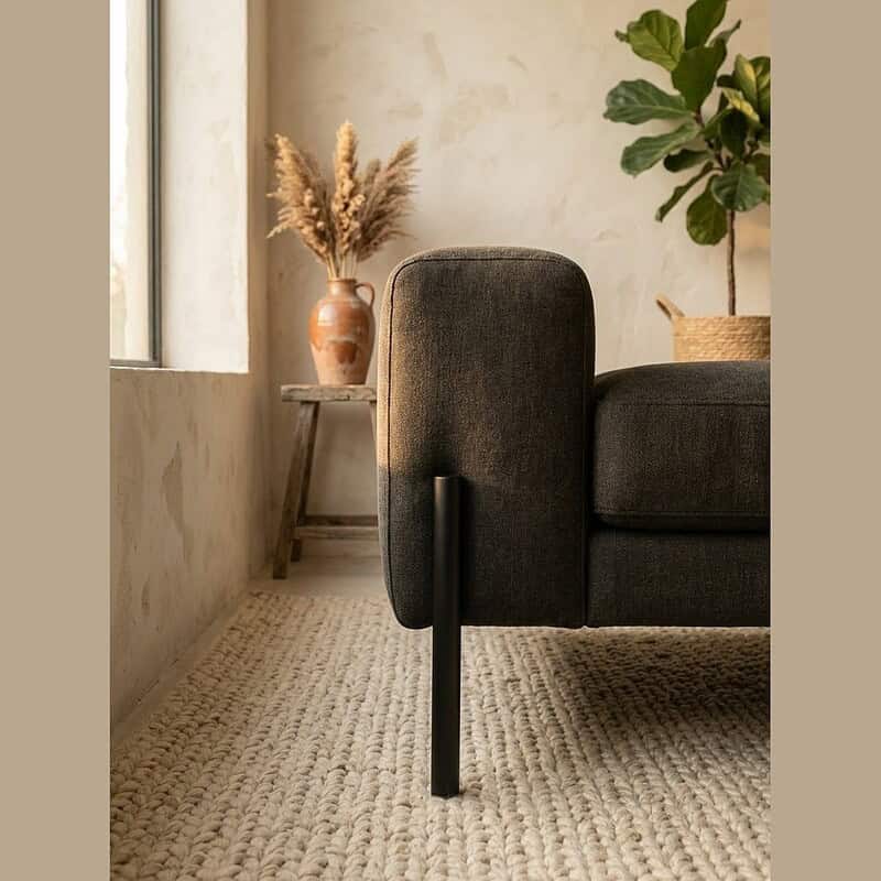 Moderne zwarte stoffen bank met houten pootjes in een lichte, minimalistische woonkamer met natuurlijke decoratie en een zachte tapijtvloer.
