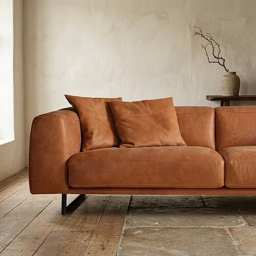 Luxe cognackleurige leren bank in een minimalistische woonkamer met houten vloer en decoratieve vaas op tafel, perfect voor moderne interieurstijl.