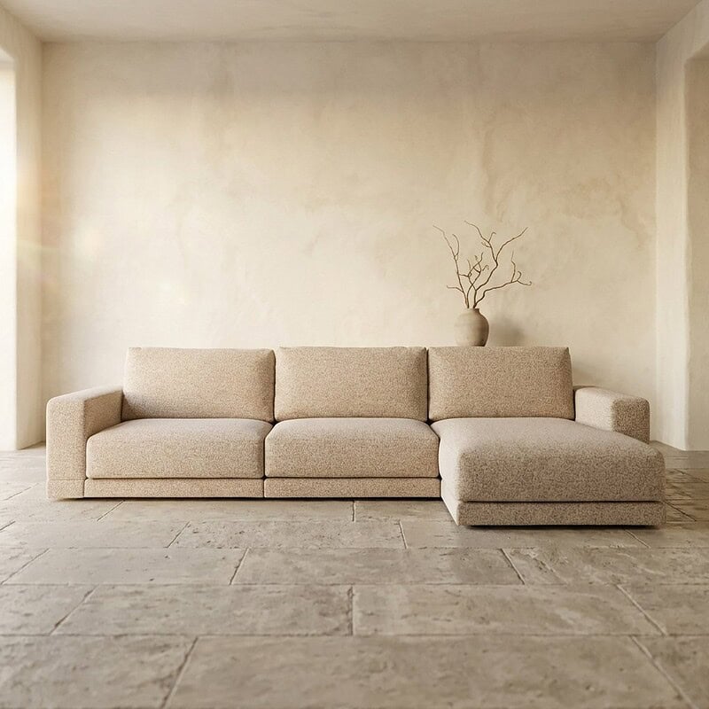 Ein modernes, beiges Ecksofa in einem schlichten, minimalistischen Wohnzimmer mit natürlichem Lichteinfall und einer schlichten Einrichtung. Perfekt für eine stilvolle und gemütliche Sitzecke.