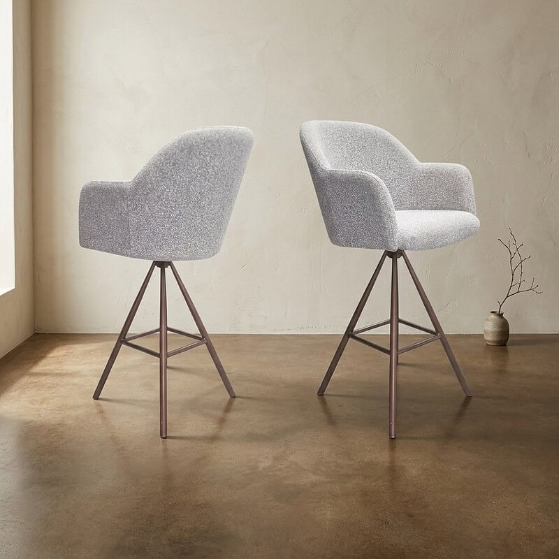 Twee moderne houten eetkamerstoelen met zachte, lichtgrijze bekleding en elegante armleuningen, geplaatst in een minimalistische interieursetting.