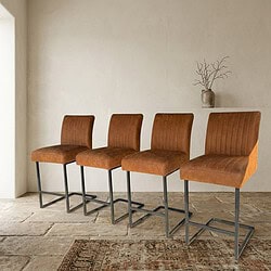 Vier stijlvolle barkrukken met bruin leren zittingen en zwarte metalen poten, geplaatst in een minimalistische interieurruimte. Perfect voor een moderne keuken of bar.