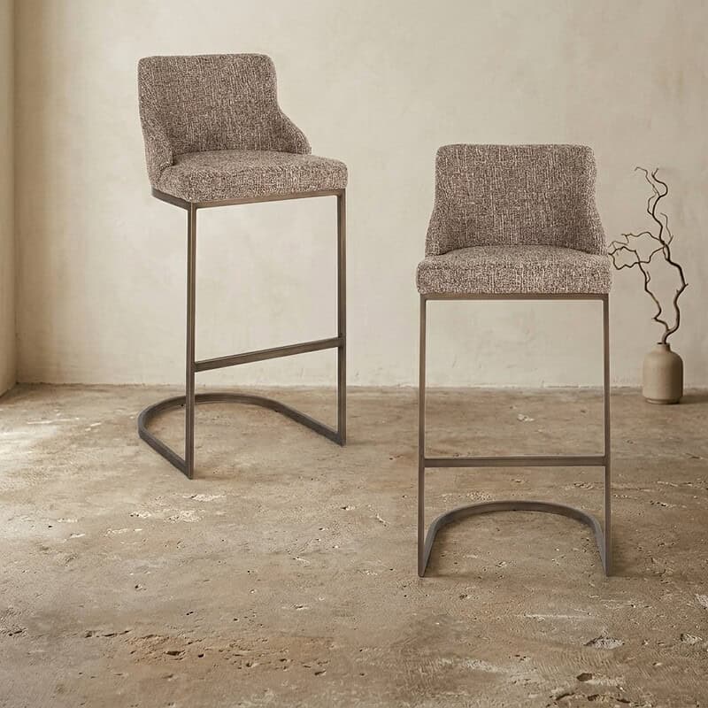 Moderne hoge barkrukken met stoffen zitting en metalen frame, geschikt voor keukeneilanden en bars, in een minimalistisch interieur.