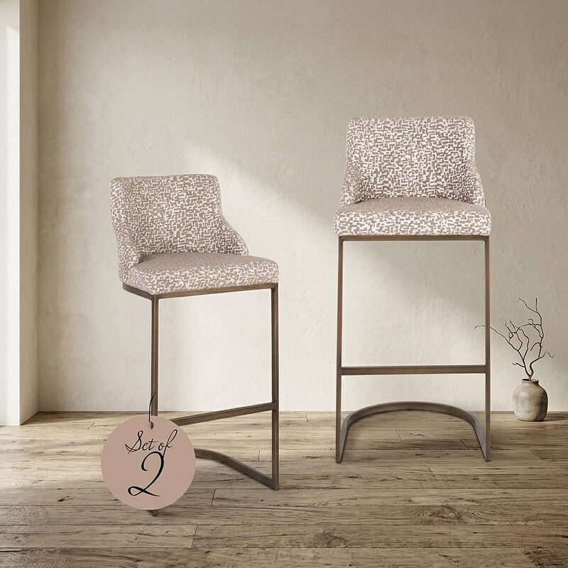 Twee stijlvolle barkrukken met gestoffeerde zittingen en metalen frame, ideaal voor eetkamers of bars, in een moderne en elegante uitstraling.