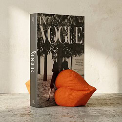 Vintage Vogue magazine en een oranje gestoffeerde fauteuil op houten tafel, decoratief en stijlvol, perfect voor interieur- of meubelfotografie.