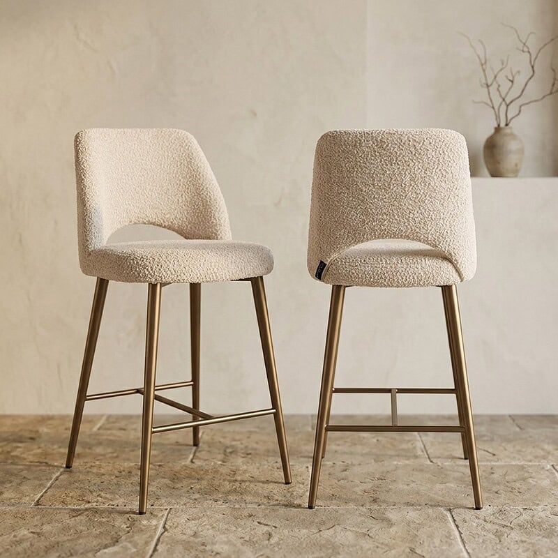 Twee moderne eetkamerstoelen met zachte crème bekleding en goudkleurige poten, perfect voor een stijlvolle en comfortabele eetruimte.