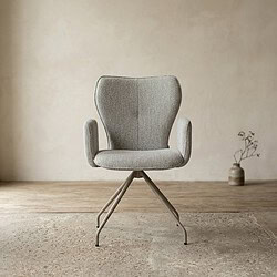 Moderne Mokana designstoel met comfortabele armleuningen en metalen onderstel, geplaatst in een minimalistisch interieur met een vaas en plant op de achtergrond.