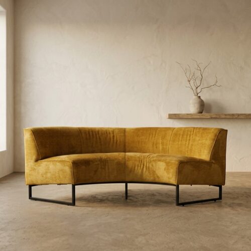 Elegante gele velvet bank van Mokana Meubelen in een minimalistisch interieur met een neutrale muur en een decoratieve vaas op een plank. Perfect voor een stijlvolle woonkamer.