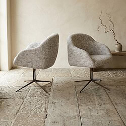 Twee moderne stoffen lounge stoelen met draaibare onderstellen, geplaatst op een landelijke stenen vloer in een minimalistische interieursetting.