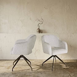 Twee moderne witte zitstoelen met gebogen armleuningen en zwarte metalen poten, geplaatst in een minimalistische interieursetting met een beige muur en een decoratieve vaas op de achtergrond.