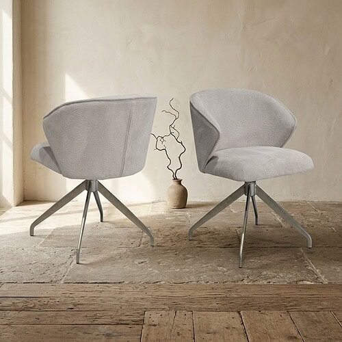 Twee moderne houten eetkamerstoelen met zachte, lichtgrijze bekleding en metalen poten, geplaatst in een minimalistische interieursetting.