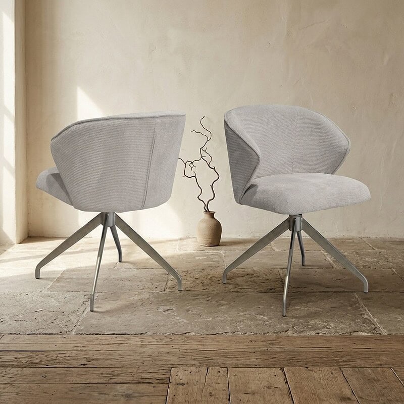 Twee moderne houten eetkamerstoelen met zachte, lichtgrijze bekleding en metalen poten, geplaatst in een minimalistische interieursetting.