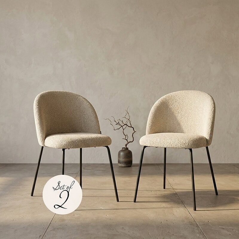 Zwei beige Sessel mit schwarzen Metallbeinen im minimalistischen Design, platziert in einem hellen Wohnzimmer mit einer dekorativen Vase und Zweigen.
