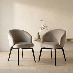 Zwei moderne skandinavische Esszimmerstühle mit weicher Polsterung und schwarzen Beinen, platziert in einem minimalistischen Interieur.