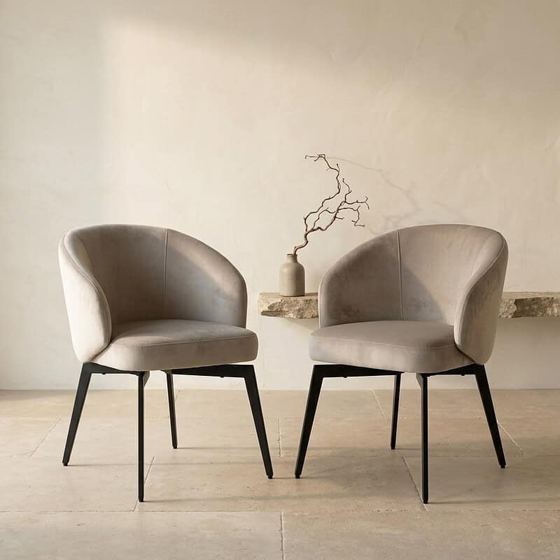 Zwei moderne skandinavische Esszimmerstühle mit weicher Polsterung und schwarzen Beinen, platziert in einem minimalistischen Interieur.