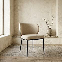 Moderne eetkamerstoel met beige stoffering en zwarte metalen poten, geplaatst in een minimalistische interieursetting met een vintage vaas en takken op de achtergrond.