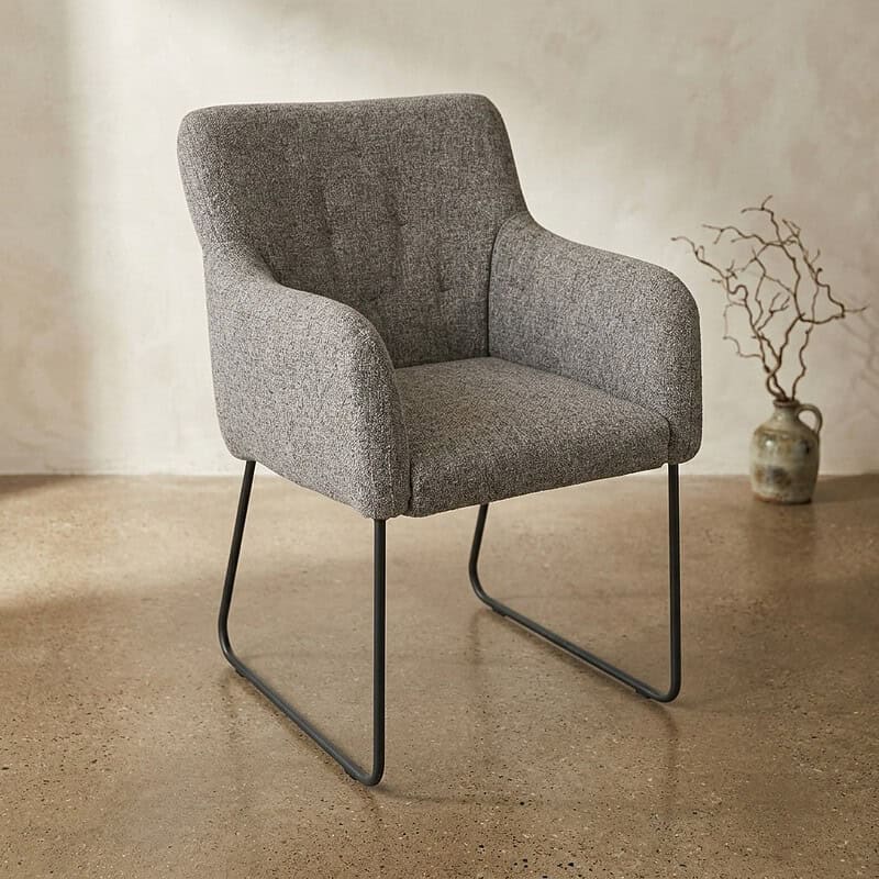 Moderne houten armstoel met zachte stoffen bekleding en slanke metalen poten, ideaal voor een stijlvolle en comfortabele zithoek in huis of kantoor.
