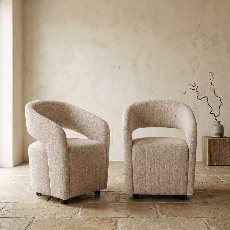 Twee moderne fauteuils in beige stof, geplaatst in een minimalistische woonkamer met een natuurlijke uitstraling en eenvoudige decoratie.