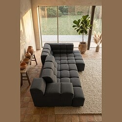 Moderne L-vormige bank in donkergrijze stof, perfect voor een stijlvolle en comfortabele zithoek in een woonkamer met grote ramen en natuurlijke decoratie.