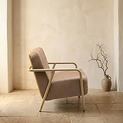 Moderne fauteuil met beige bekleding en metalen armleuningen, geplaatst in een minimalistische interieursetting met een keramieken vaas en een tak in de achtergrond.