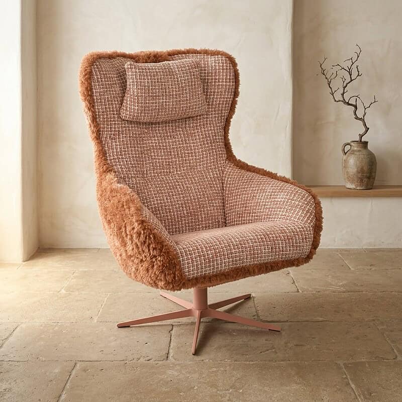 Comfortabele fauteuil met hoge rugleuning en kussens, bekleed met zachte stoffen, geplaatst in een rustige, minimalistische interieurruimte met een decoratieve vaas op de achtergrond.