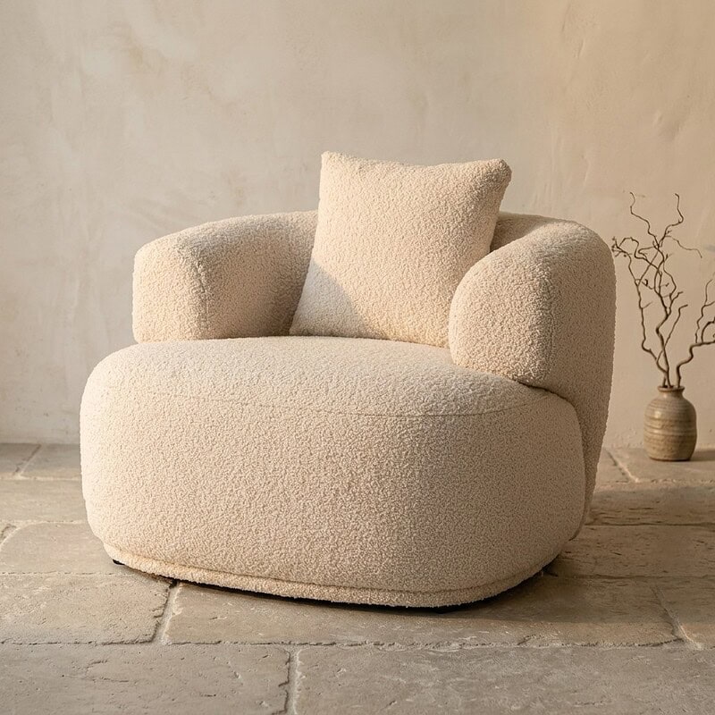 Ein bequemer, weicher Stoffsessel mit runden Formen und einem passenden Kissen – perfekt für eine gemütliche Sitzecke zu Hause.