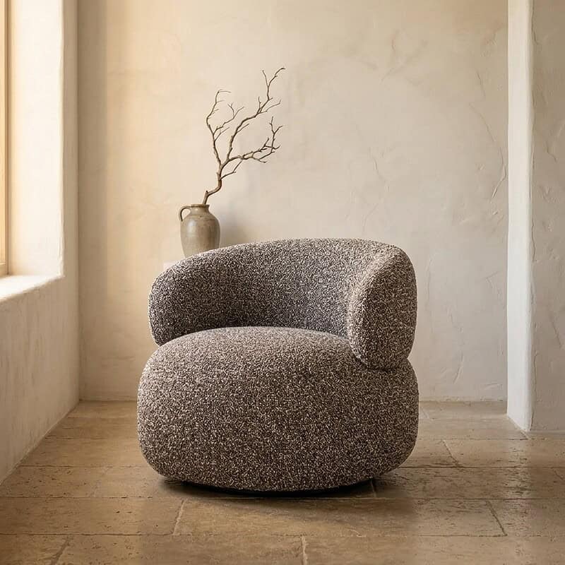 Ein bequemer, moderner Polstersessel mit runden Formen in einem minimalistischen Wohnzimmer, kombiniert mit einer dekorativen Vase und einer natürlichen Ausstrahlung.