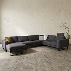 Ein modernes Loungesofa in einem minimalistischen Wohnzimmer mit grauem Stoffbezug, kombiniert mit Zierkissen und einer dekorativen Pflanze im Hintergrund.