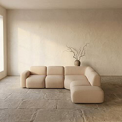 Moderne beige loungebank in een rustige, minimalistische woonkamer met natuurlijke lichtinval en een decoratieve vaas met takken op de achtergrond.