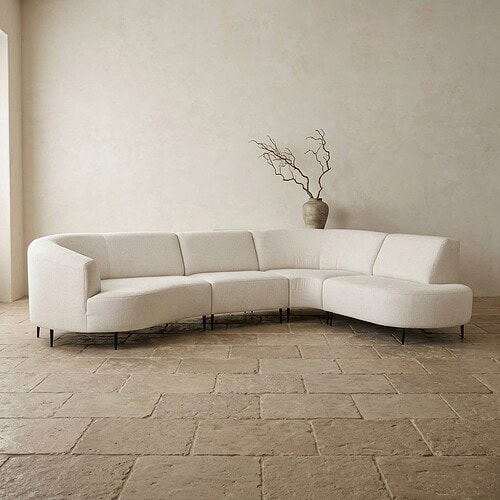 Moderne witte hoekbank in een minimalistisch interieur met een vaas en takken op de achtergrond, perfect voor stijlvolle woonruimtes.
