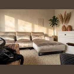 Elegante velvet hoekbank in een stijlvolle woonkamer met natuurlijke lichtinval, perfect voor comfortabel loungen en moderne interieurdecoratie.