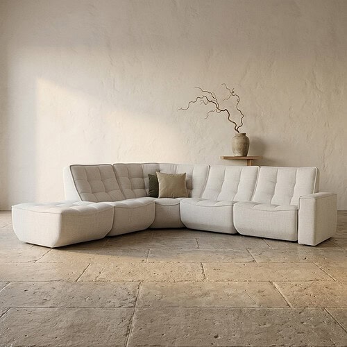 Moderne L-vormige bank in lichte stof met decoratieve kussens, perfect voor een stijlvolle woonkamer. Gemaakt door Mokana Meubelen, bekend om hoogwaardige en op maat gemaakte meubels.