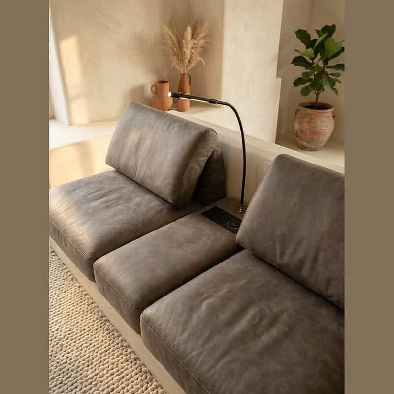 Moderne grijze stoffen bank met geïntegreerde leeslamp en groene kamerplant, perfect voor een stijlvolle en comfortabele woonkamer.