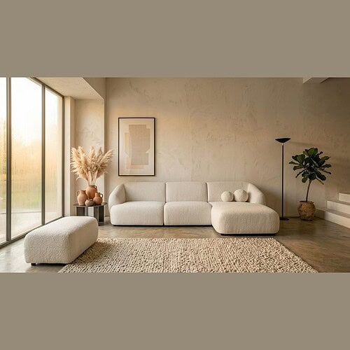 Moderne woonkamer met witte bank, poef, planten en decoratieve elementen in een lichte, minimalistische ruimte met grote ramen en natuurlijke lichtinval.