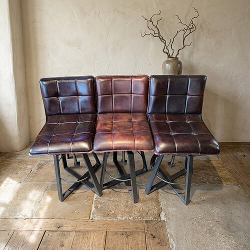 Drei Esszimmerstühle aus Leder mit Metallbeinen, passend für moderne Esszimmer in einem rustikalen Einrichtungsstil.