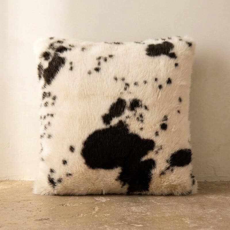 Luxe koeienhuid kussen in zwart-wit patroon, perfect voor een moderne of landelijke interieurstijl, toegevoegd aan een houten vloer voor een gezellige sfeer.
