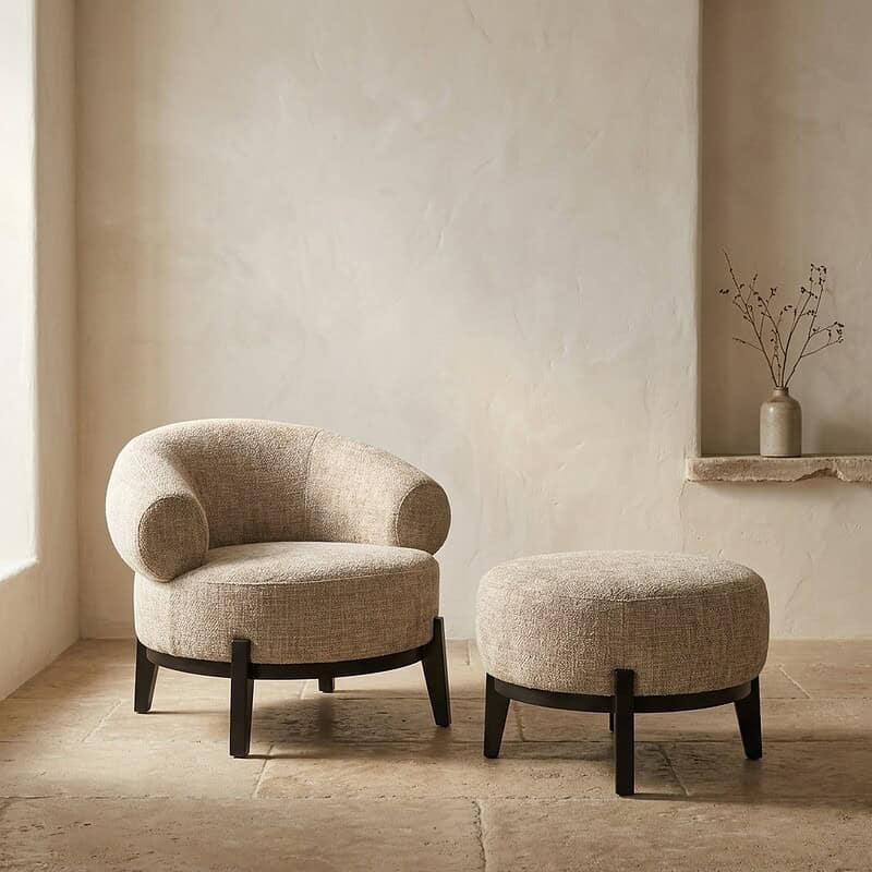 Luxe beige lounge stoel en bijpassende poef, perfect voor een stijlvolle en comfortabele zithoek in huis. Gemaakt van hoogwaardig textiel met zwarte houten poten.