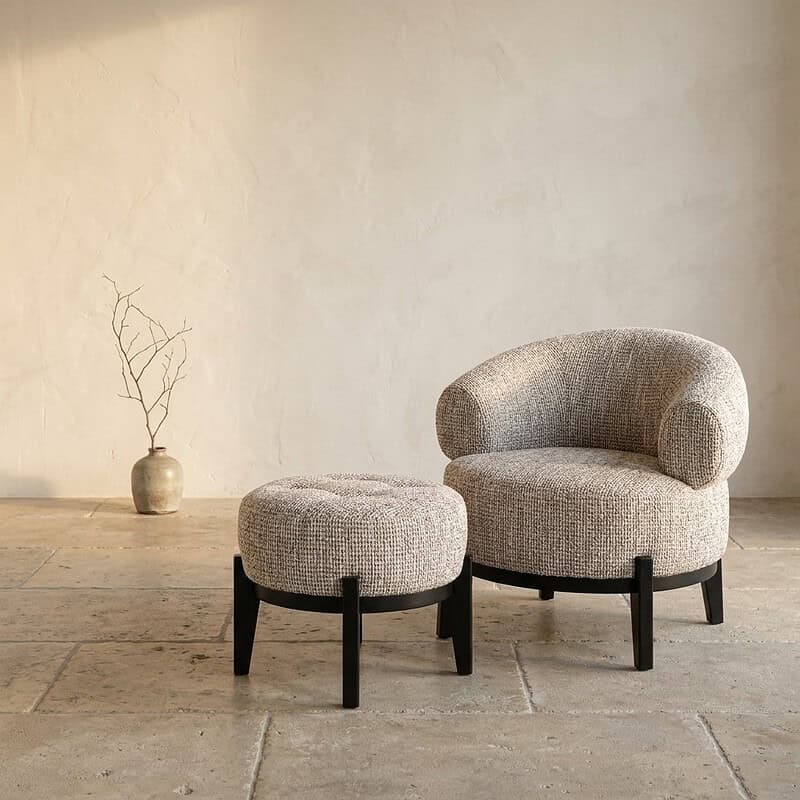 Luxe Mokana lounge stoel en bijpassende ottoman, modern design met zachte stoffen bekleding en zwarte houten poten, perfect voor stijlvolle zithoeken.