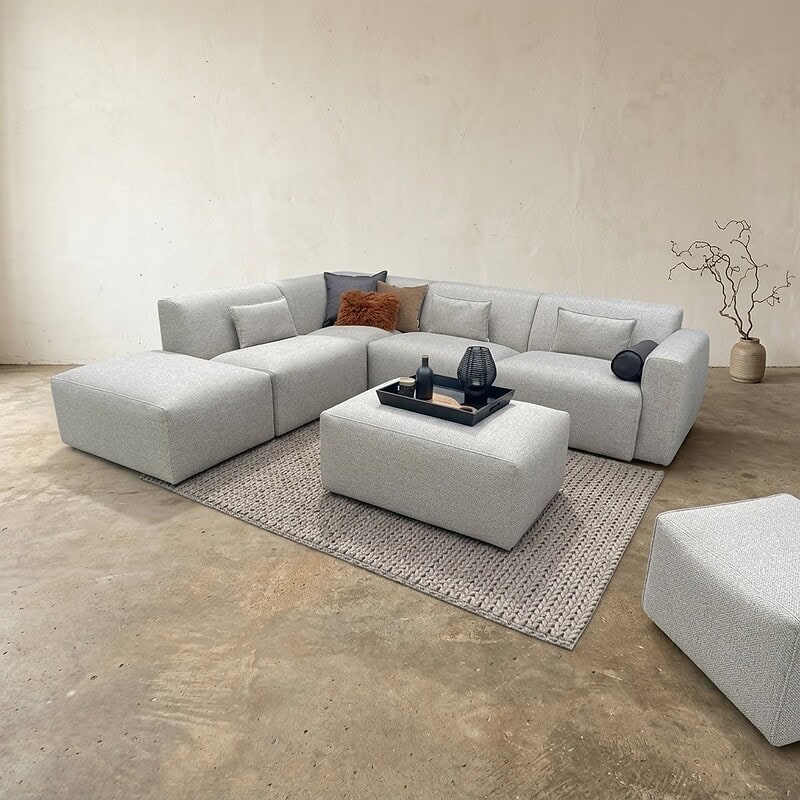Moderne Lounge-Ecke mit Möbeln von Mokana, bequemer Eckcouch und passendem Hocker, im minimalistischen Einrichtungsstil.