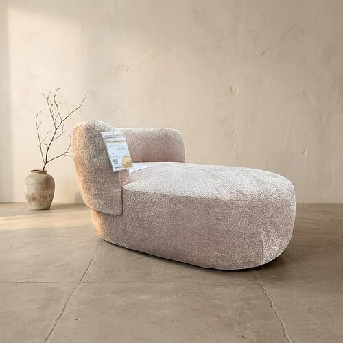 Luxe zachte fauteuil met uniek ontwerp, perfect voor modern interieur, bekleed met comfortabel lichtroze stof, geplaatst in een minimalistische woonkamer.