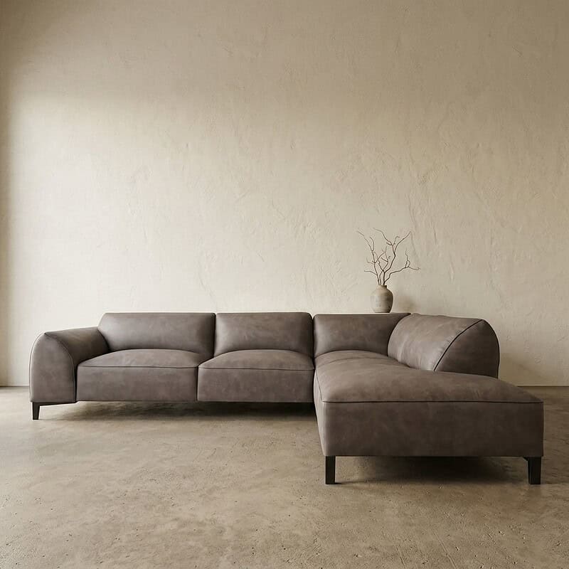 Moderne grijze leren bank met chaise longue in minimalistisch interieur, geschikt voor stijlvolle woonkamers.