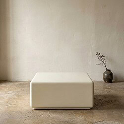 Moderne witte bank in een minimalistisch interieur met een ruwe betonvloer en een eenvoudige vaas met takken op de achtergrond, perfect voor een strak en eigentijds woonconcept.