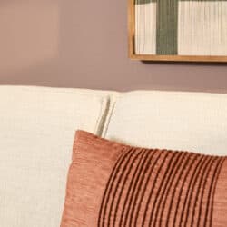 Woonkamerbank met beige bekleding en rustieke kussen, modern interieur met muurkunst en houten lijst.