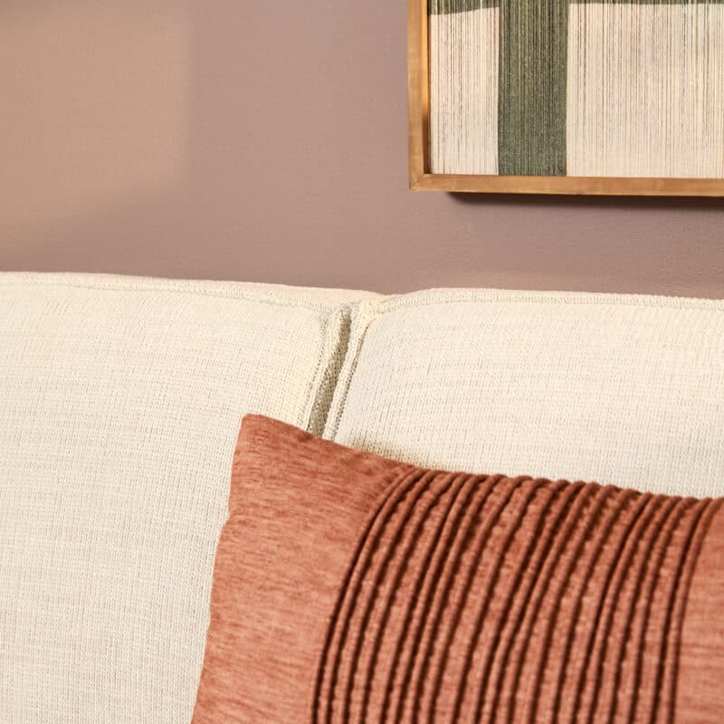 Comfortabele beige divan met kussen en decoratief kunstwerk op de muur, perfect voor een gezellige woonkamer.