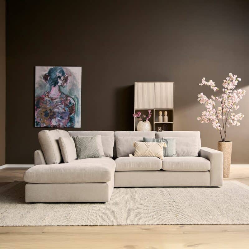 Lichte woonkamerbank met meerdere kussens in een modern interieur met kunstwerk en bloemen.