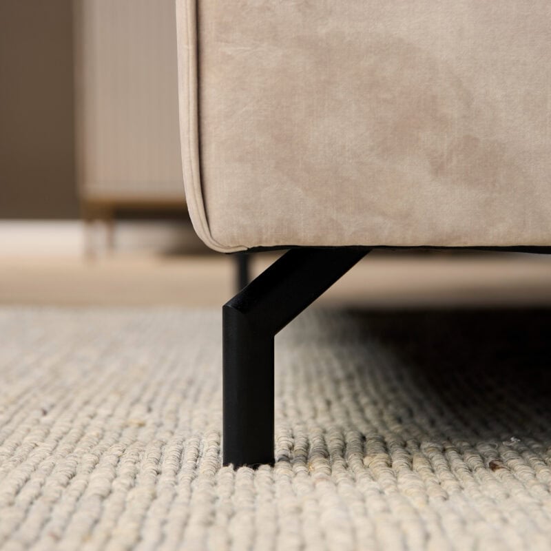 Close-up van een beige lounge fauteuil met zwarte metalen poot, perfect voor moderne woonkamers.